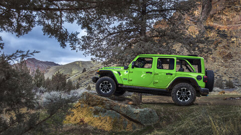 Bright green Jeep Wrangler Rubicon off-roading on rocky terrain in the mountains.