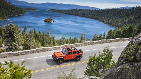 Red Jeep Wrangler driving near a lake