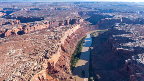 Aerial view of a winding river cutting through red rock canyons in the desert landscape.