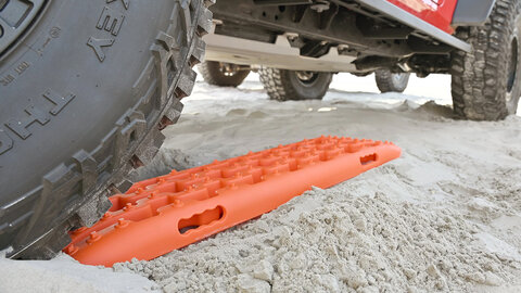 Orange Jeep recovery boards in the sand under a Jeep.