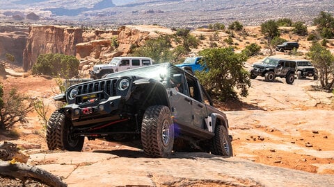 Gray Jeep climbing a rock ledge with a desert background